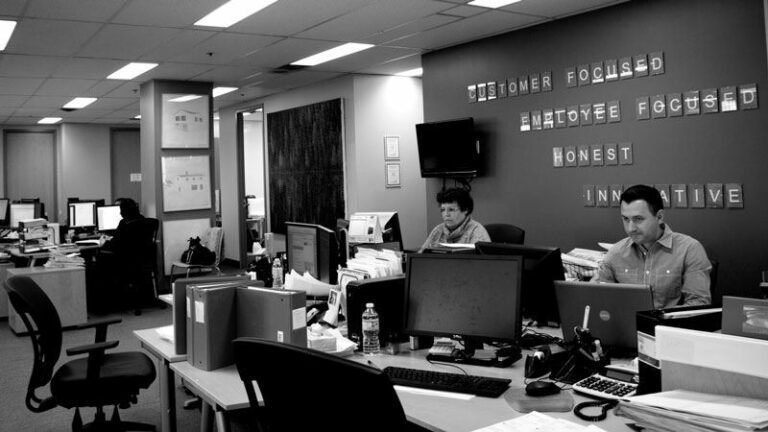 Benecaid office. People working on computers at their desks. "Customer focused, employee focused, honest, innitiative" written on the wall.